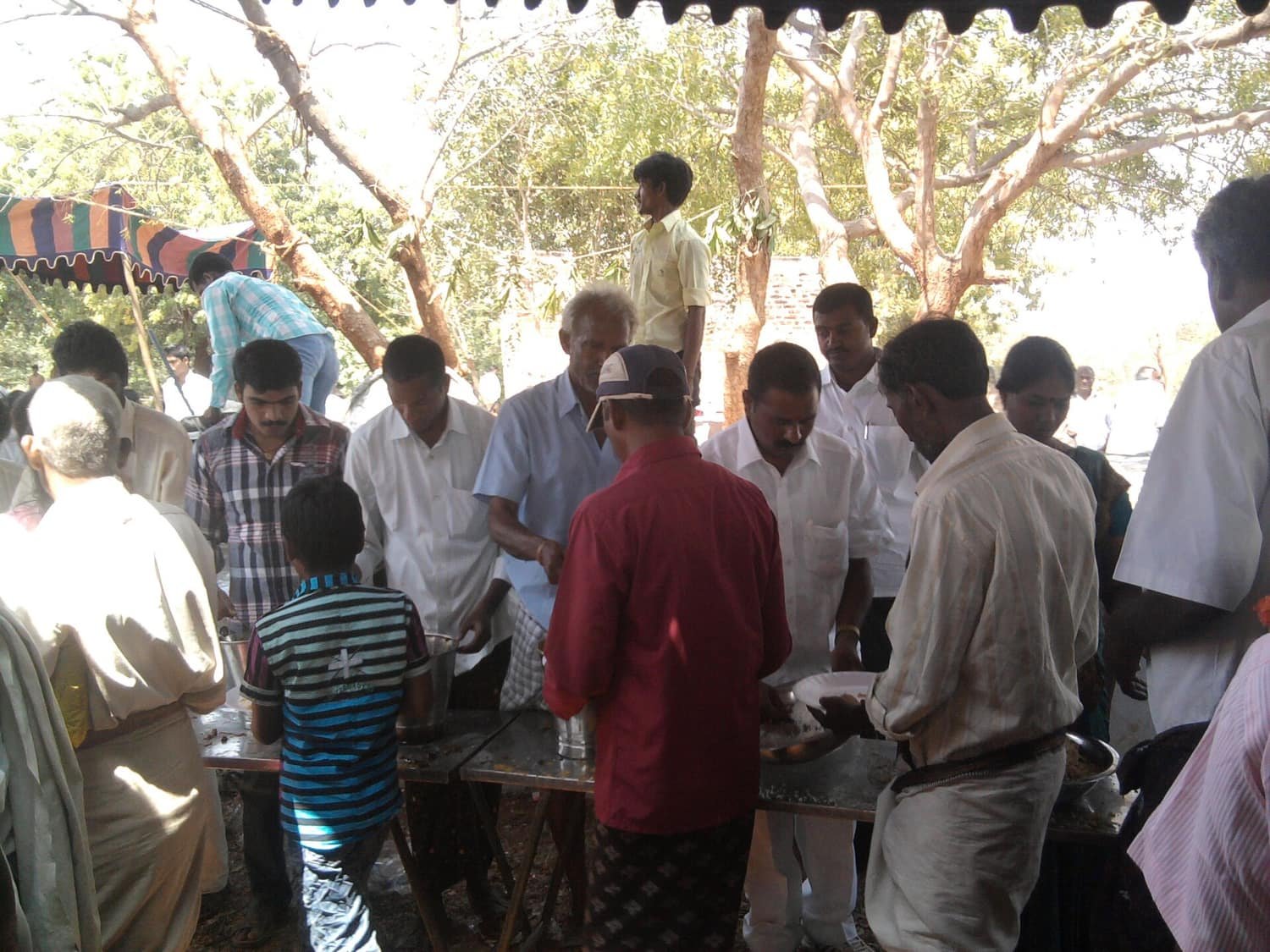 People being served a communal meal outdoors under trees